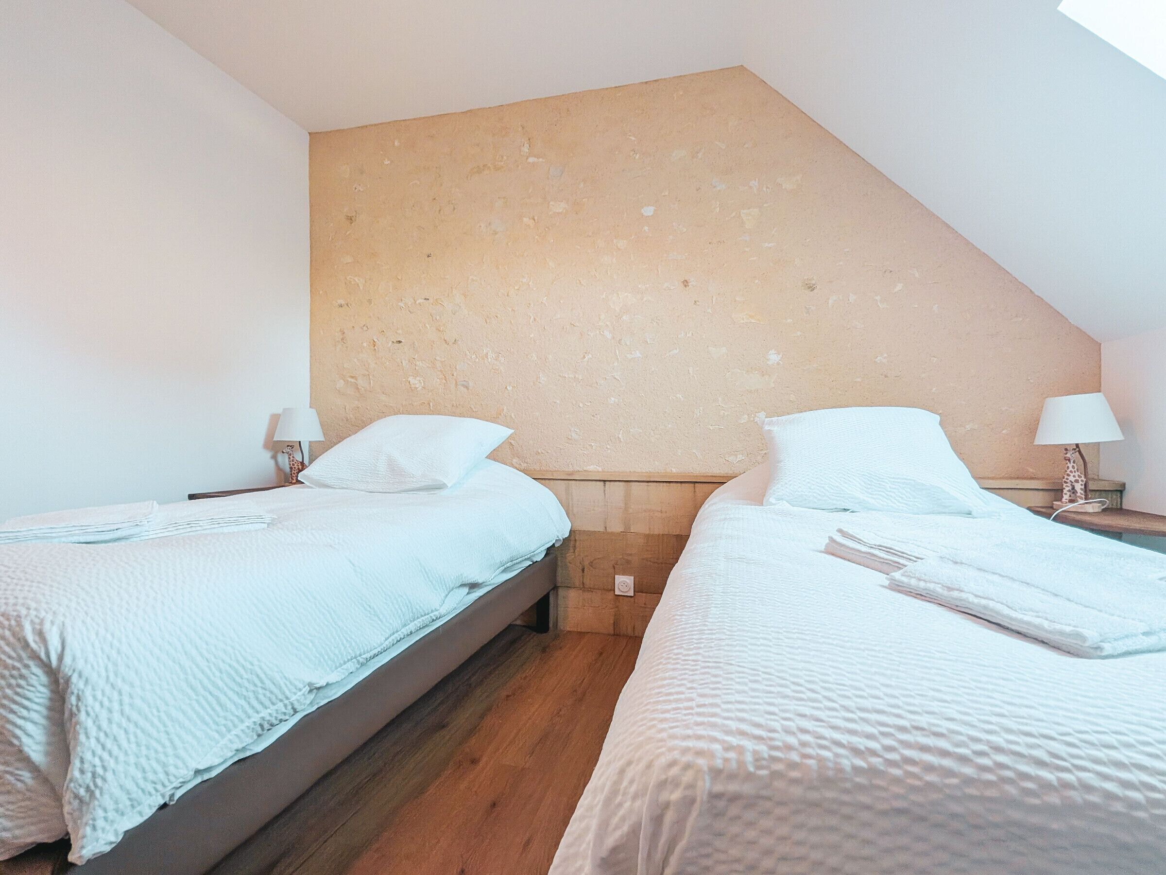 Una camera da letto con due letti, ognuno con copripiumino e cuscini bianchi, e pavimento in legno.