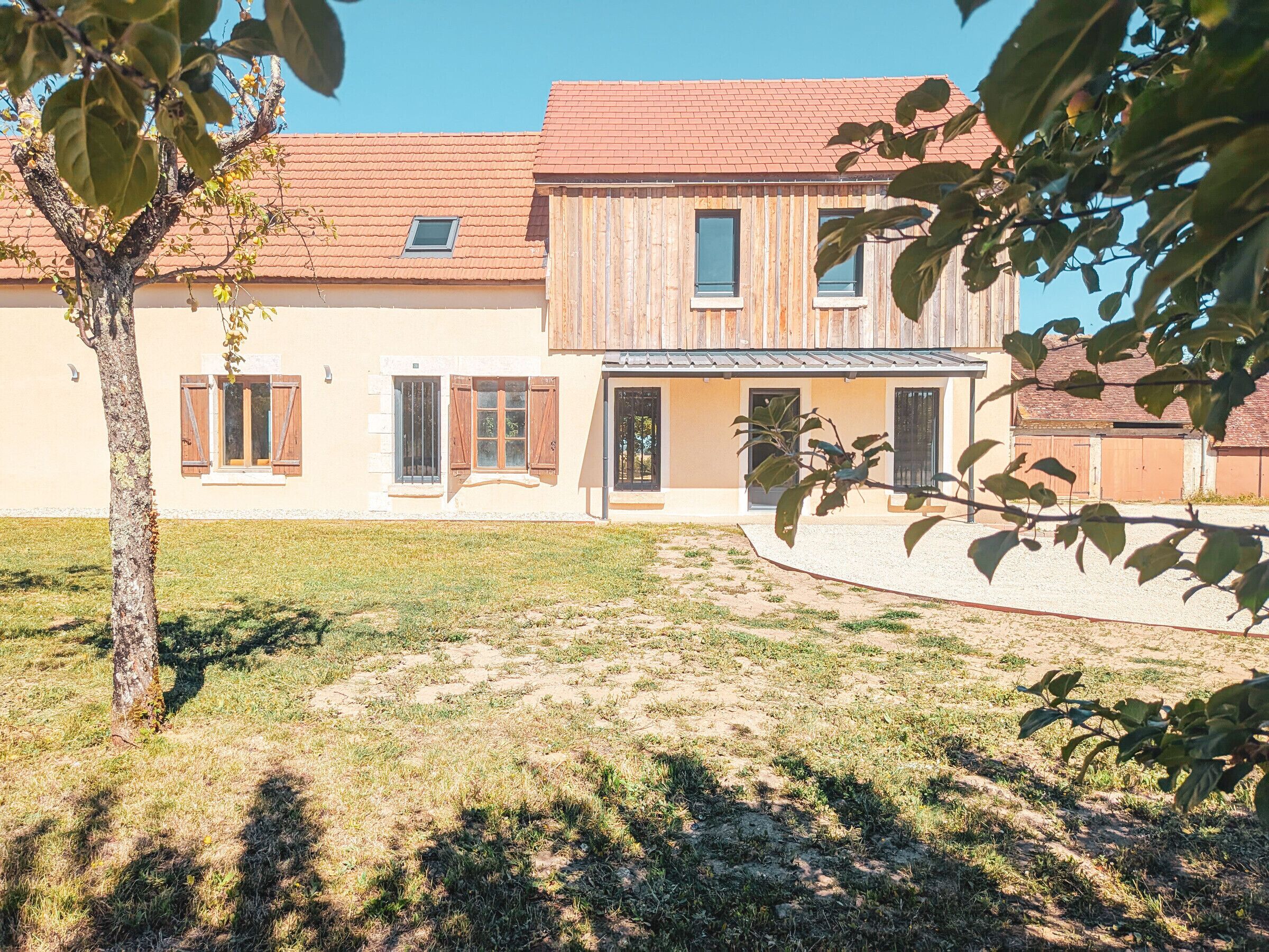 Ein zweistöckiges Haus mit rotem Ziegeldach, Holzläden an den Fenstern und einer kleinen Veranda.