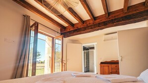 Een slaapkamer met een groot bed, een houten garderobe en een glazen deur naar een douchegedeelte.