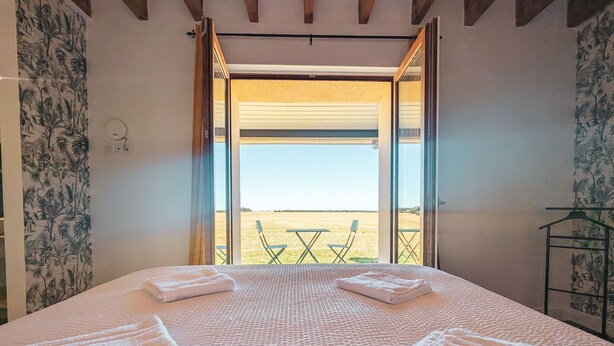 Een slaapkamer met een groot bed, twee handdoeken, een raam en uitzicht op een veld.