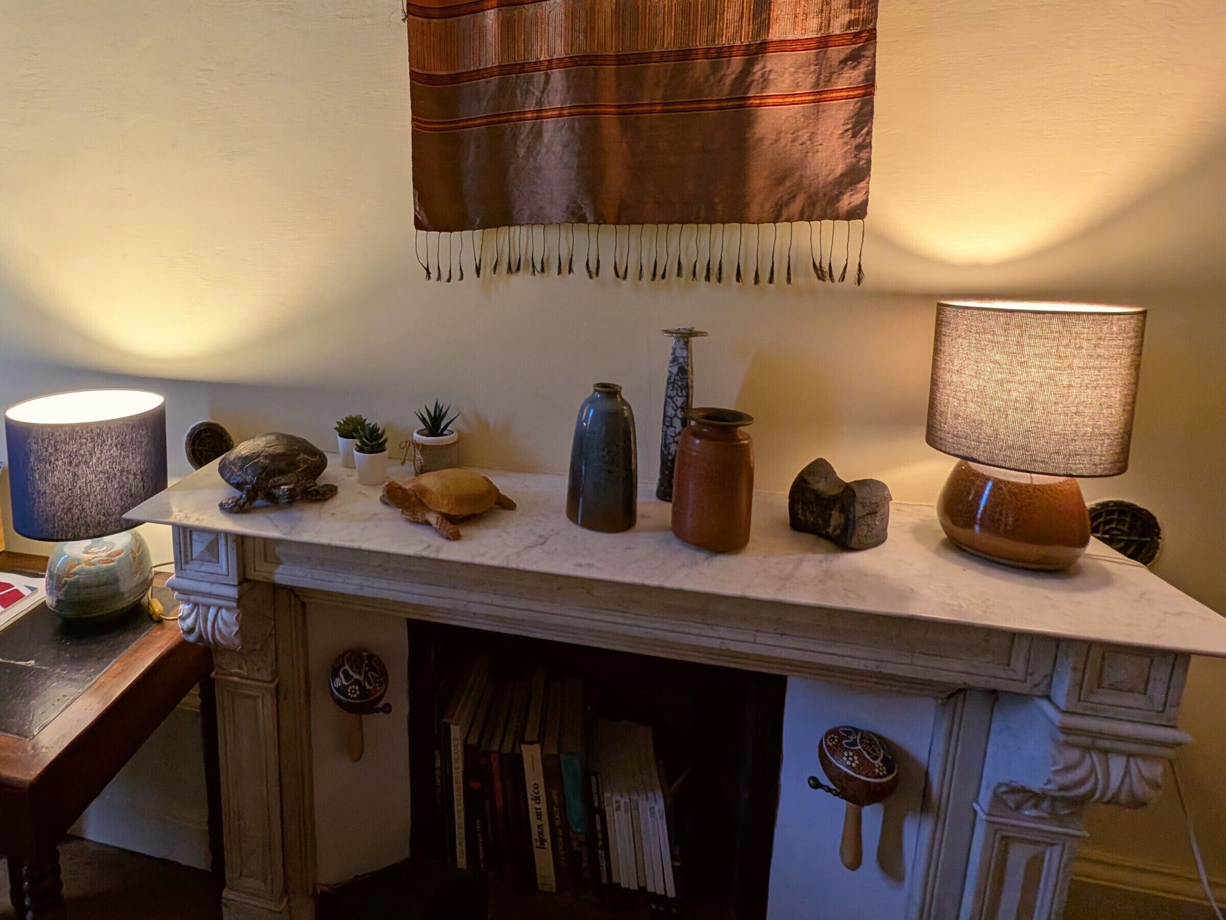 A fireplace mantel with decorative items, a lamp, and a hanging tapestry.