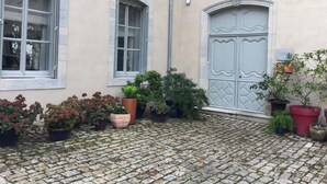 A cobblestone courtyard with potted plants and a building with a large blue door and windows.