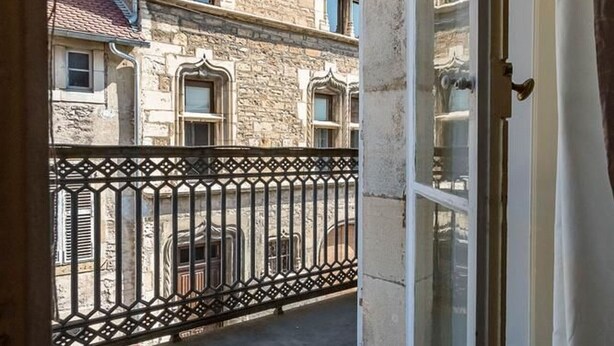 A view from a balcony with a wrought iron railing, stone building facade, and a window with a white frame.