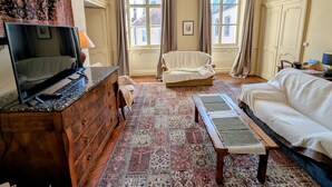 A traditional room with a wooden dresser, a television, a patterned rug, a white sofa, and a bed.