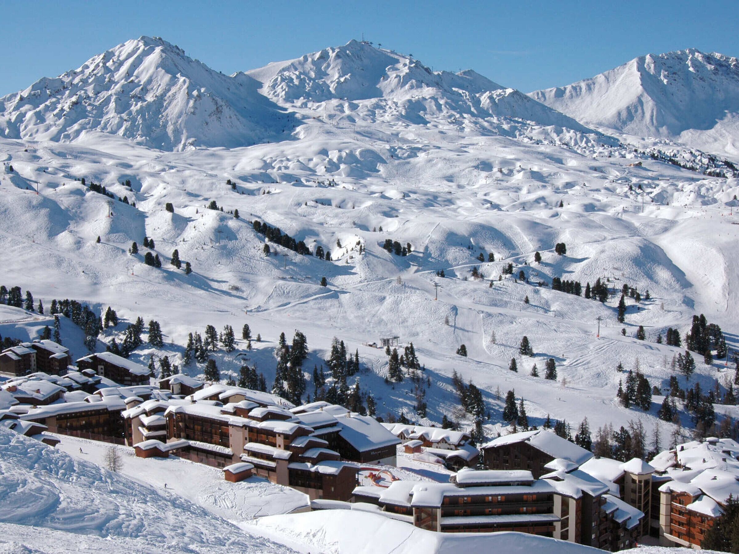 Et snedækket feriested med flere bygninger, ski slopes og en klar himmel.