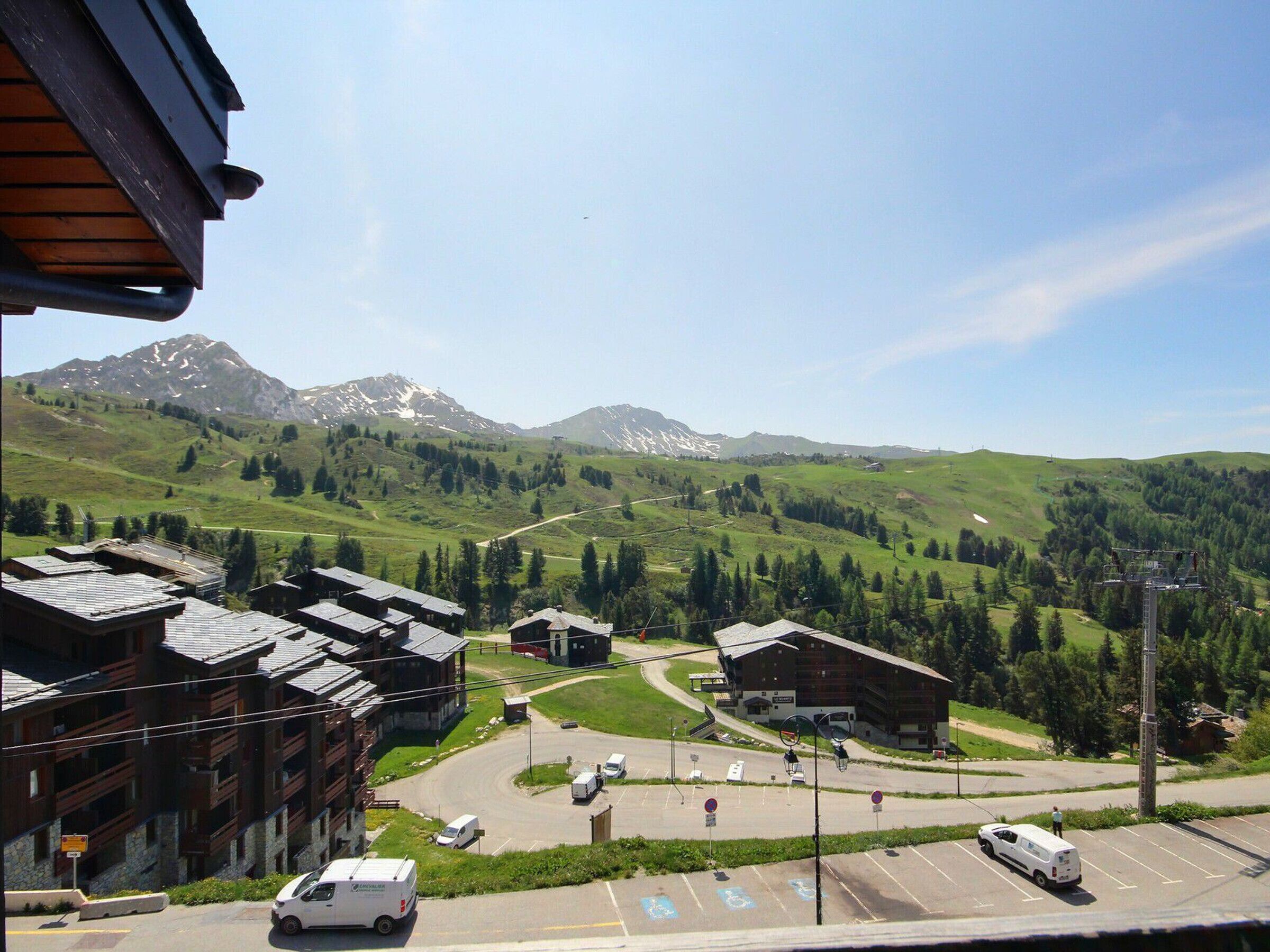 Un complejo turístico de montaña con edificios de estilo chalet, un área de estacionamiento y un telesilla al fondo.
