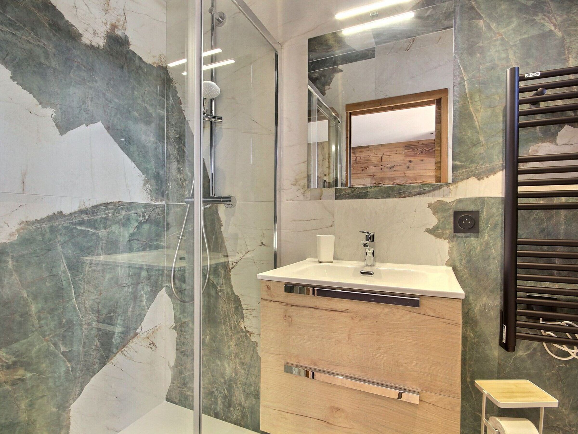 A modern bathroom with a glass-enclosed shower, a wooden vanity, and a marble wall.