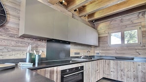 A modern kitchen with wooden walls, a built-in oven, and a window. - New chalet with jacuzzi and sauna (La Plagne)