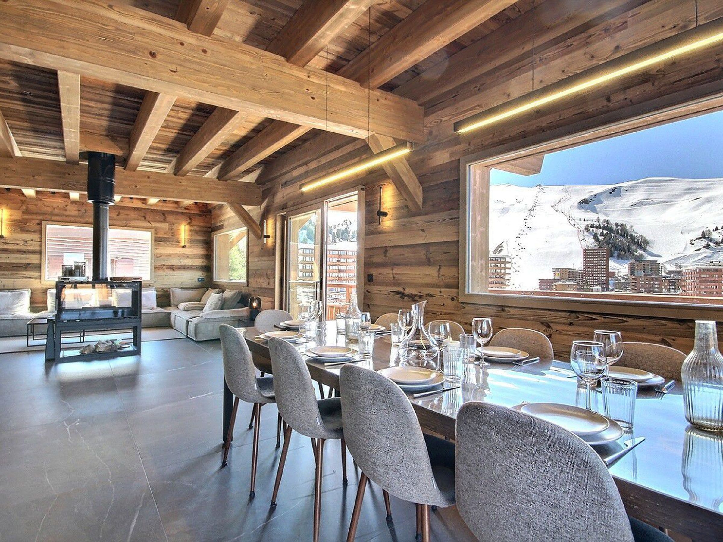 A wooden interior with a dining area, a fireplace, and a large window with a mountain view.