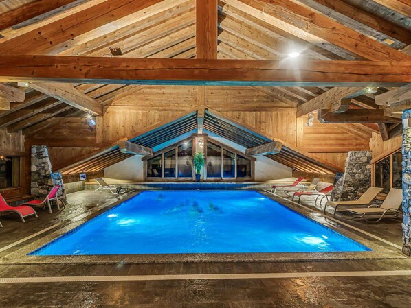 A large indoor swimming pool with a sloped ceiling and wooden beams, surrounded by lounge chairs and stone walls. - Champagny-en-Vanoise, Duplex for 8, Premium Comfort, Wifi and Garage (Champagny-en-Vanoise)