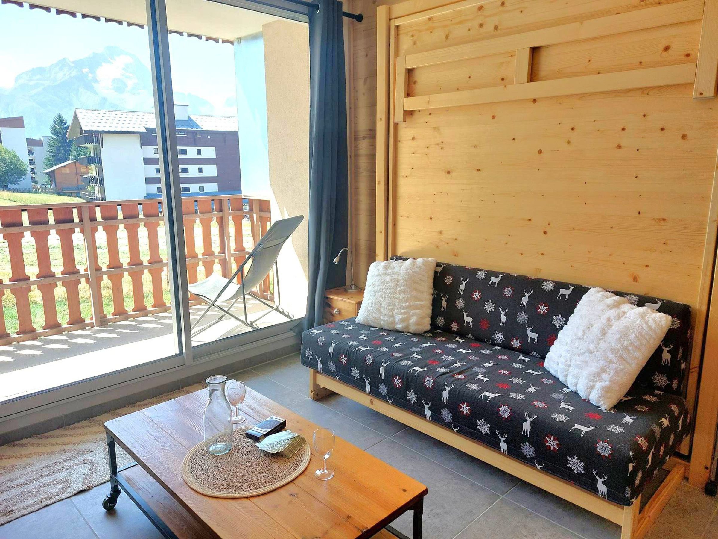 A cozy room with a wooden sofa, a small table with a glass, and a view of a balcony with a wooden fence.