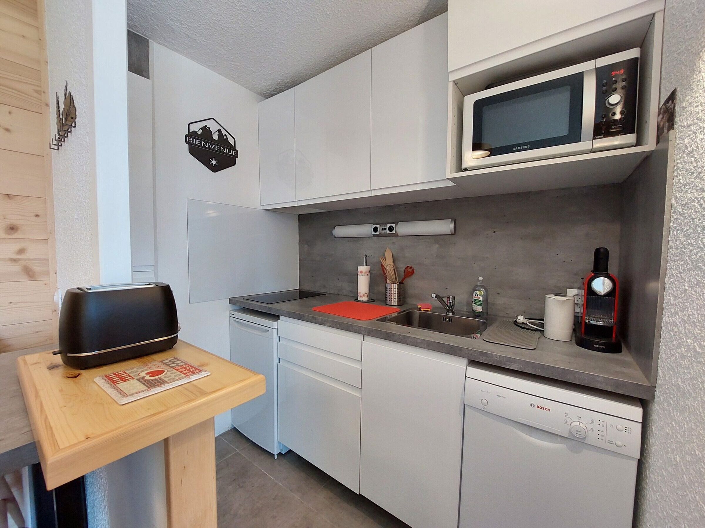 Una cocina moderna con armarios blancos, un microondas, un lavavajillas Bosch y un tostador sobre una mesa de madera.