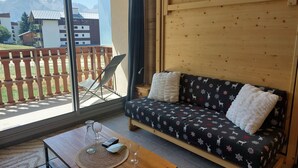 Una habitación acogedora con un sofá de madera, una mesita con una jarra de vidrio y una copa de vino, y vistas a la montaña a través de amplios ventanales.