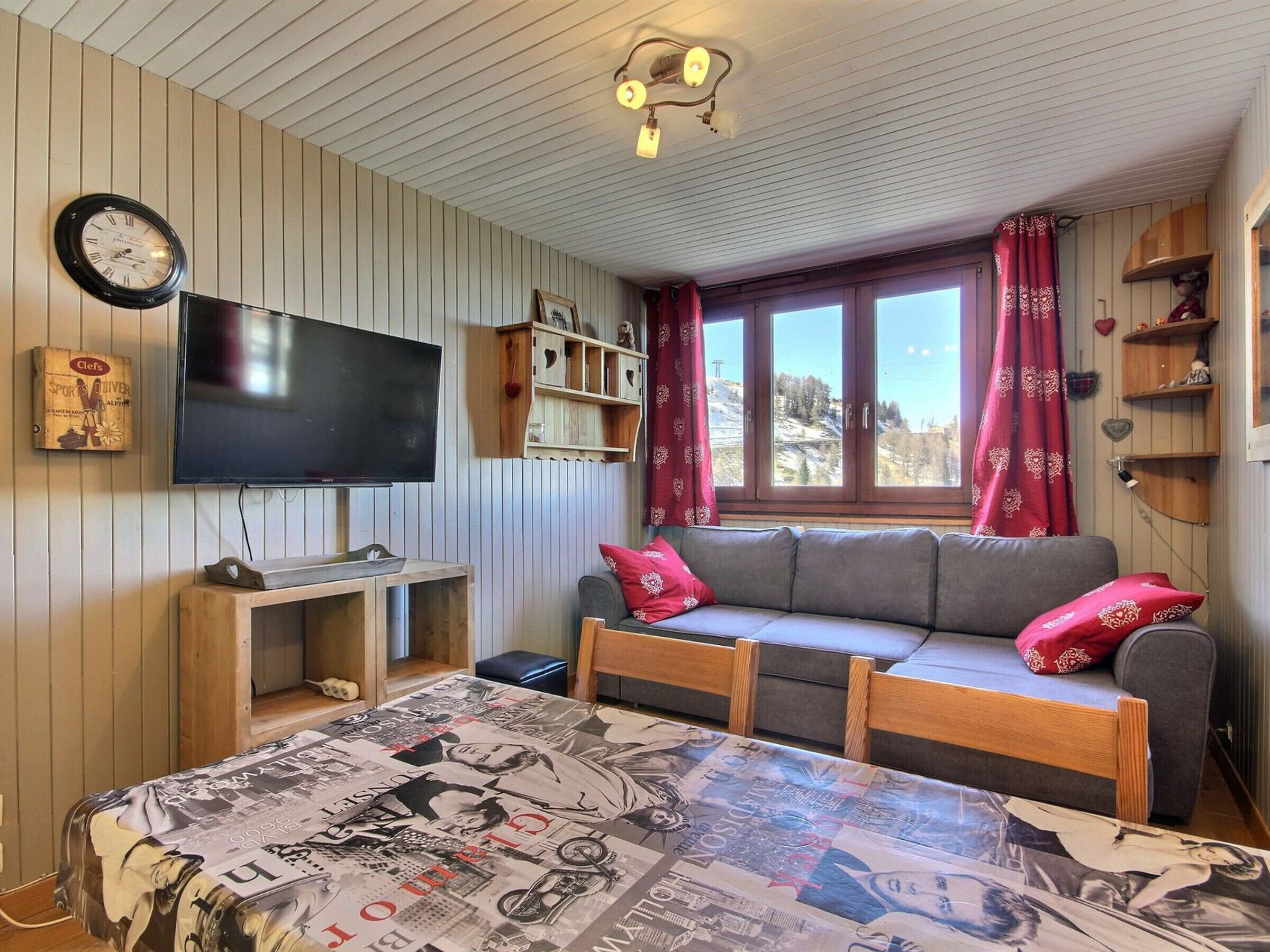 A cozy room with a television, wooden shelves, a sofa, and a window with curtains.