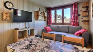 A cozy room with a television, wooden shelves, a sofa, and a window with curtains.