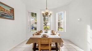 Une salle à manger avec une grande table dressée pour six personnes, des murs blancs et un lustre.