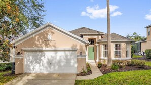 Une maison de plain-pied avec une façade de couleur beige, une porte de garage blanche et une porte d’entrée verte.