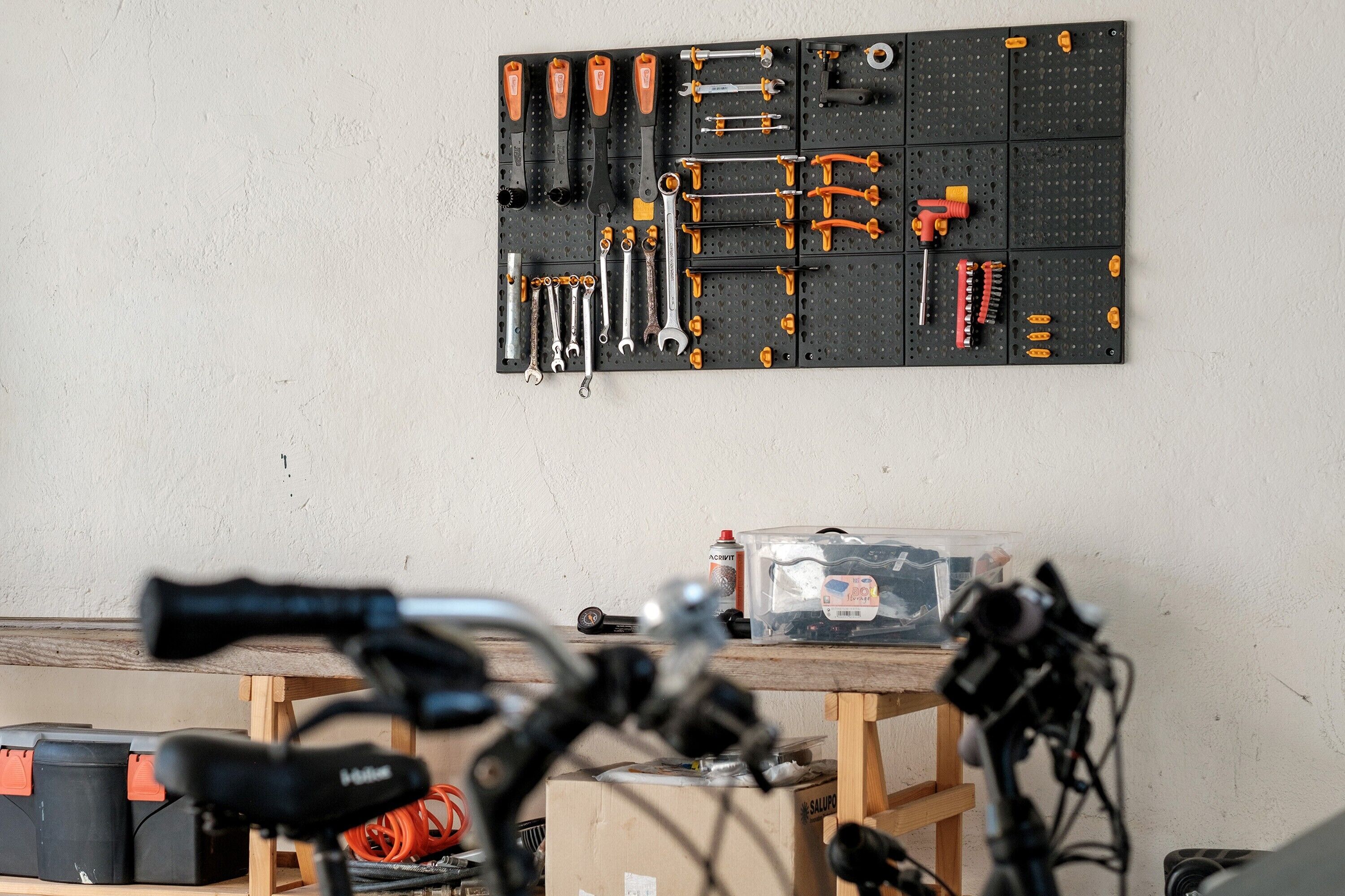 Un panneau perforé avec des outils et un établi avec des boîtes, le tout surmonté d’un vélo en premier plan.