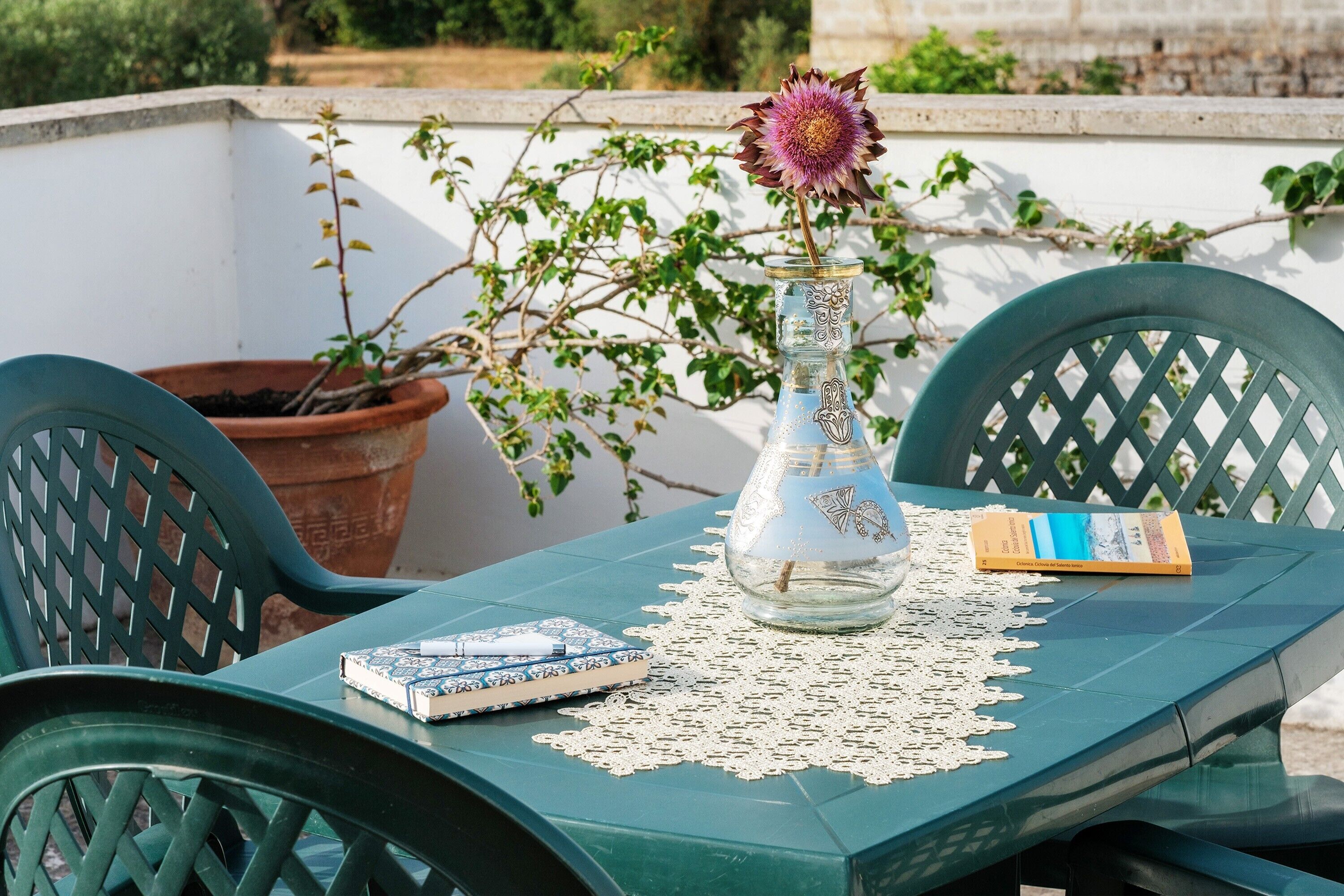A table with a book, a decorative glass vase with a flower, and a potted plant.