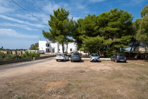 A parking area with five cars, a white building, and surrounding trees.
