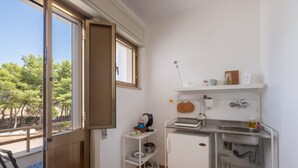 Eine kompakte Küche mit integriertem Kühlschrank, einer kleinen Spüle und einem Fenster mit Blick auf Bäume.