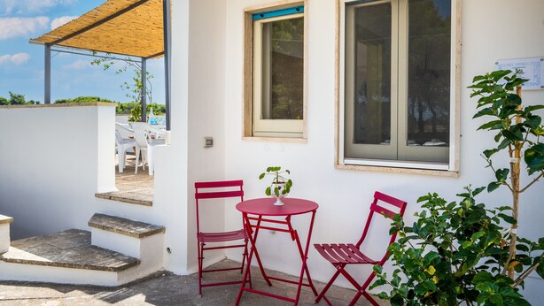Een wit gebouw met een overdekt terras, twee ramen en een kleine tafel met stoelen.