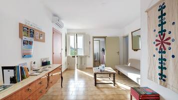 Um quarto espaçoso com piso de madeira, uma escrivaninha com livros, ar-condicionado fixado na parede e uma janela grande.