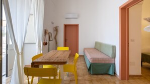 Een kamer met een houten tafel en gele stoelen, een bank met een groene kussen, en een deur met een roze frame.