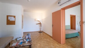 Een kamer met een bed, een tafel met tijdschriften, een lamp, een prikbord en een open deur naar een andere kamer.