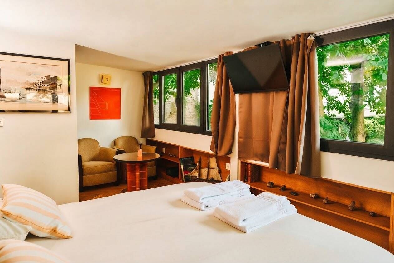 A hotel room with a bed, a desk, a chair, a television, and large windows with curtains.