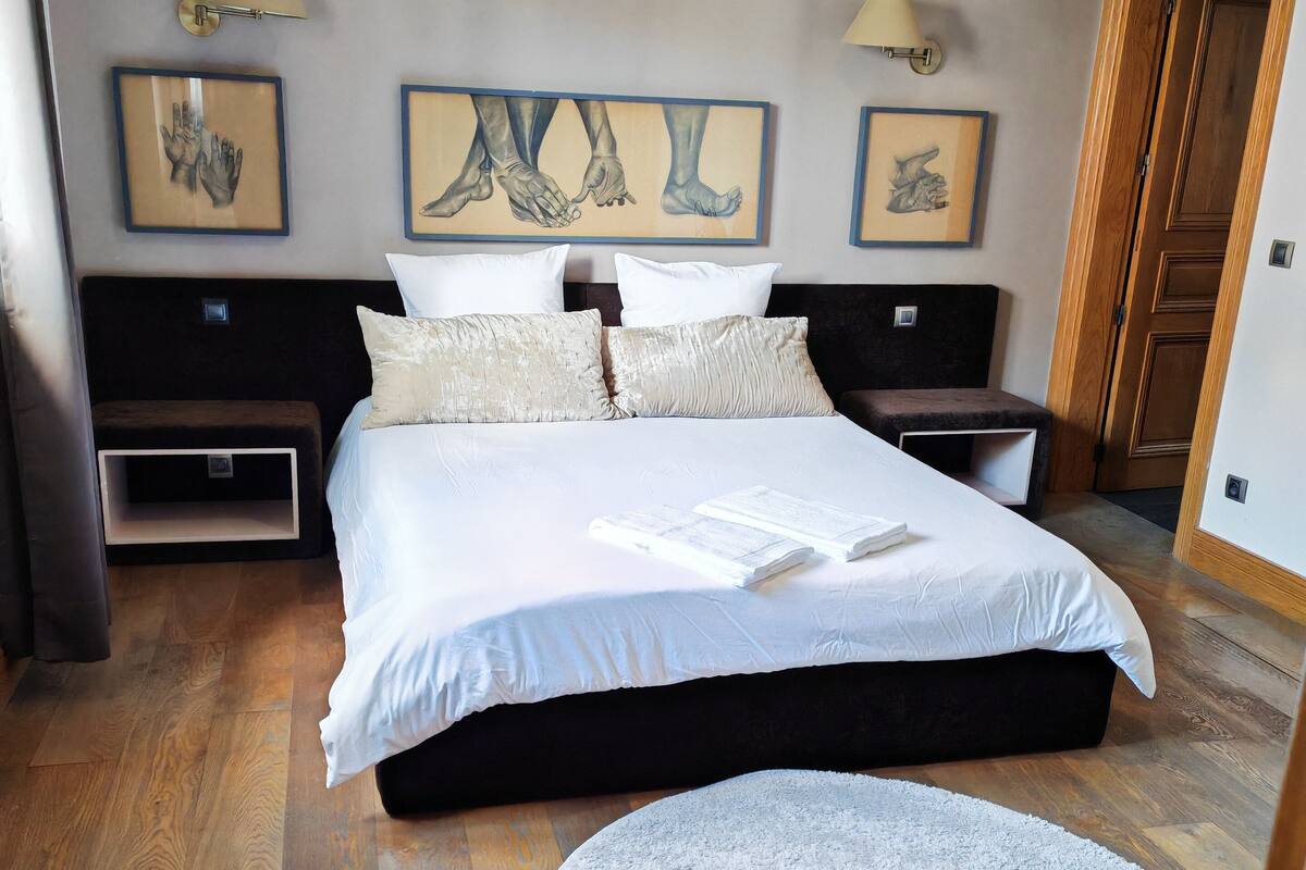 A bedroom with a large bed, two nightstands, a round rug, and artwork on the walls.