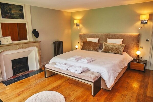 A bedroom with a large bed, bedside lamps, a fireplace, and a framed picture on the wall.