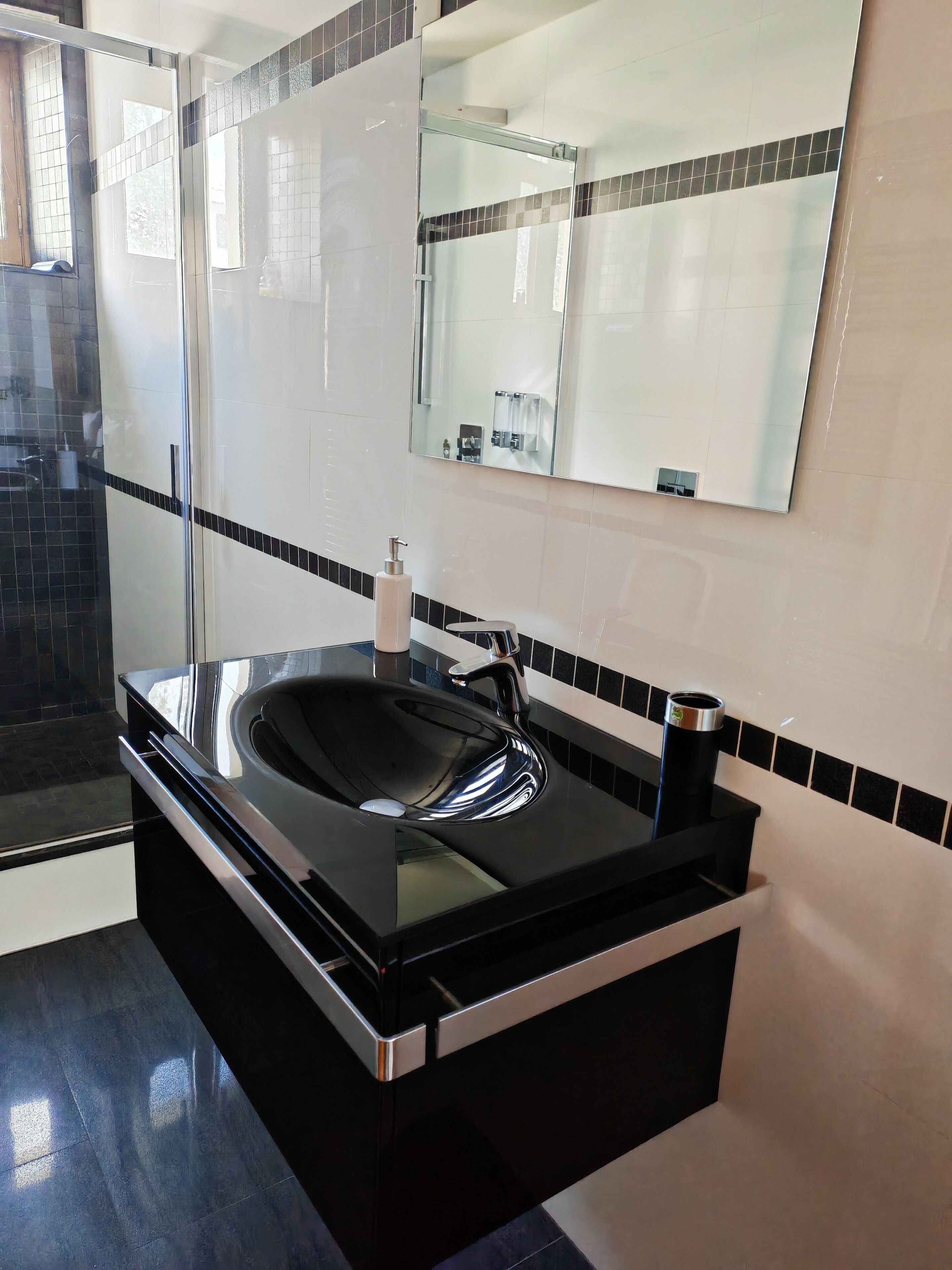 A modern bathroom with a black sink, a large mirror, and a glass shower enclosure.