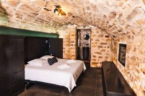 A room with a stone ceiling, a bed with white linens, a bench, and a wall-mounted TV. - villa raspail (Ivry-sur-Seine)