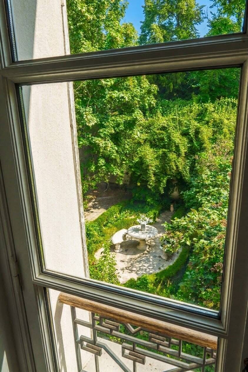 Ein Fenster mit Blick auf einen Garten, darunter eine runde Steinstruktur und üppiges Grün.