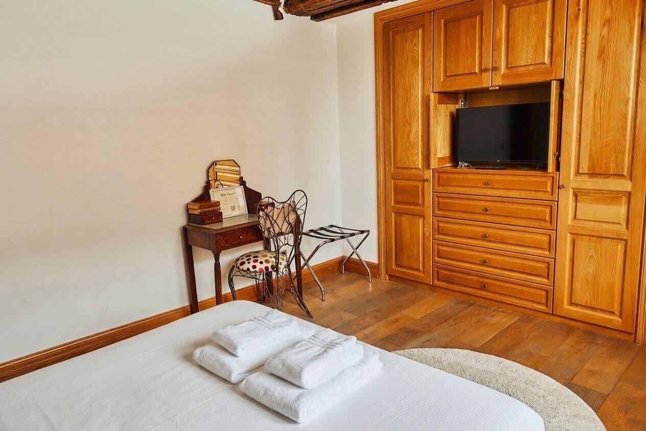 A hotel room with a bed, wooden wardrobe, a desk with a chair, and a television.