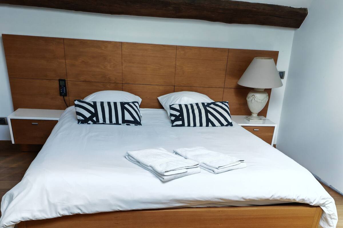 A neatly made bed with white bedding and striped pillows, a wooden headboard, and a bedside table with a lamp.