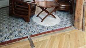 Una habitación acogedora con techo inclinado, una mesa redonda de madera, dos sillones de cuero y baldosas con diseño en el suelo.
