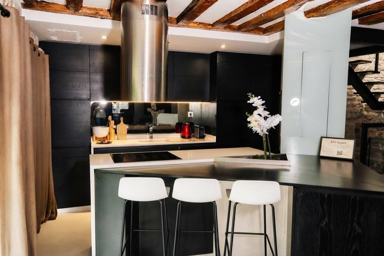 Une cuisine moderne dotée d’un îlot central, de tabourets de bar et d’une hotte de cuisine en acier inoxydable.