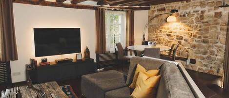 A cozy living room with a stone wall, a flat-screen TV, a sofa with cushions, a coffee table, and a lamp.