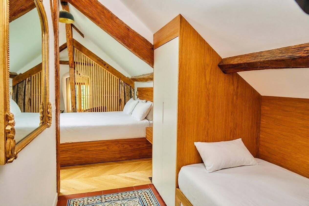Una stanza con soffitto a falde, travi in legno, un letto, un comodino e uno specchio.