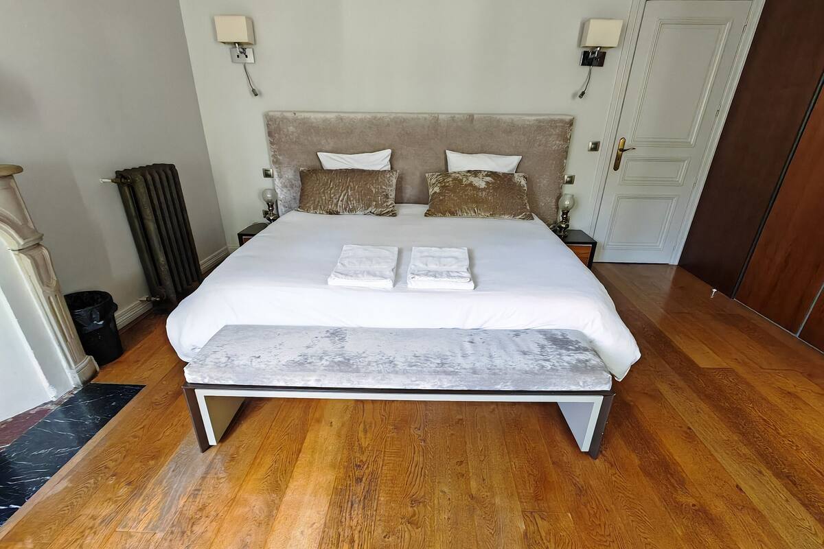 A neatly made bed with a headboard, two bedside lamps, and a wooden floor.