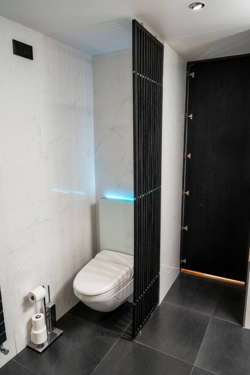 Een moderne badkamer met een wit toilet, een zwarte scheiding en een zwarte deur.