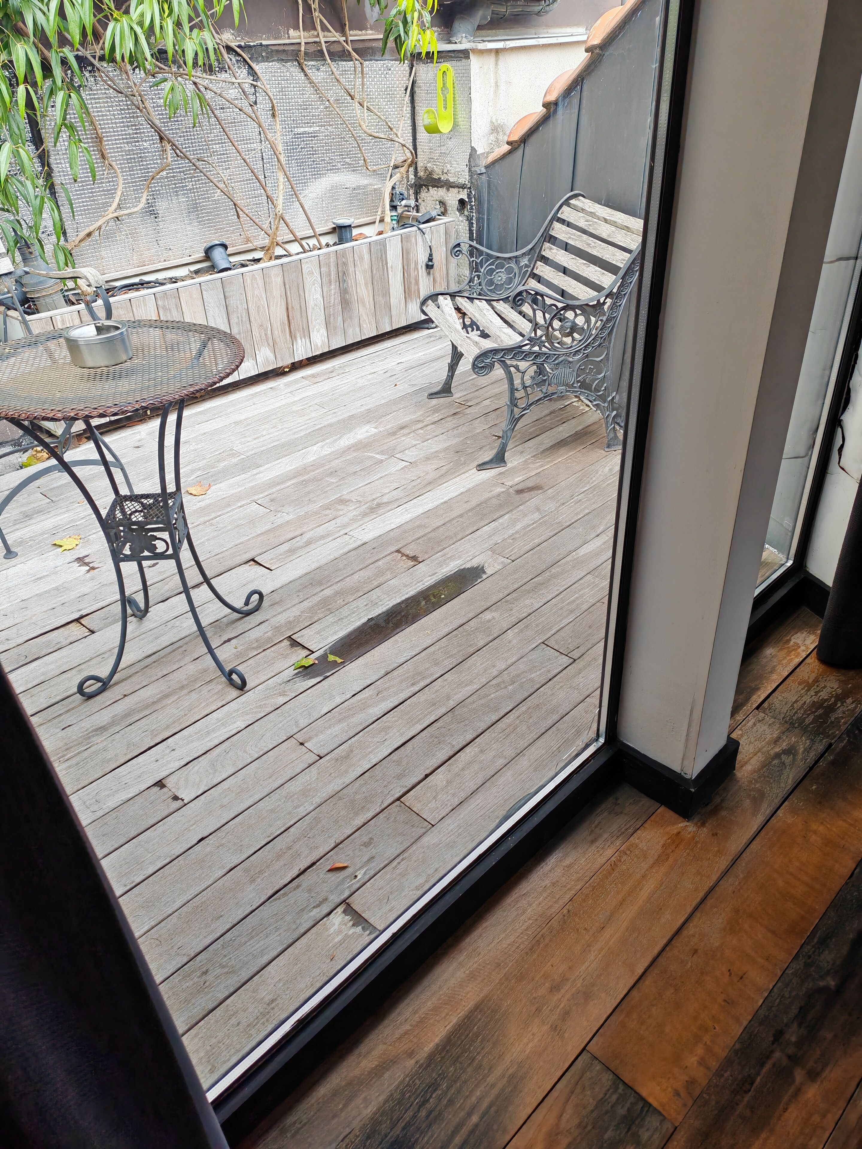 A wooden deck with a metal table and chairs, a window, and a view of a house and trees.