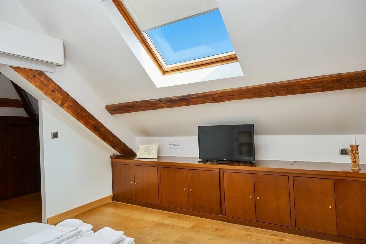 A room with a skylight, wooden beams, a television on a wooden cabinet, and a certificate on the wall.