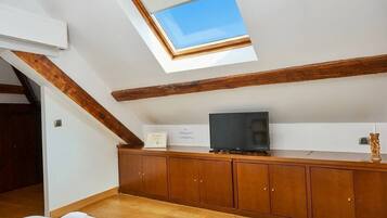 A room with a skylight, wooden beams, a television on a wooden cabinet, and a certificate on the wall.