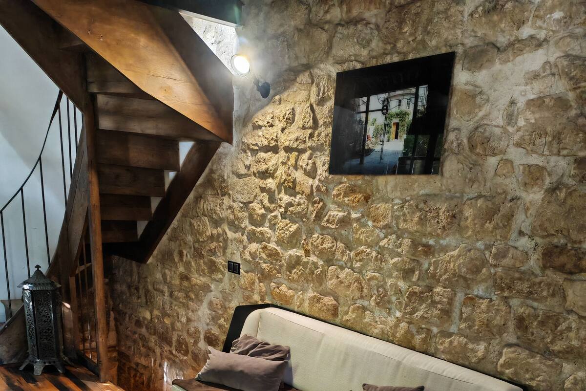 A cozy room with a stone wall, a wooden staircase, a sofa with cushions, and a marble coffee table.