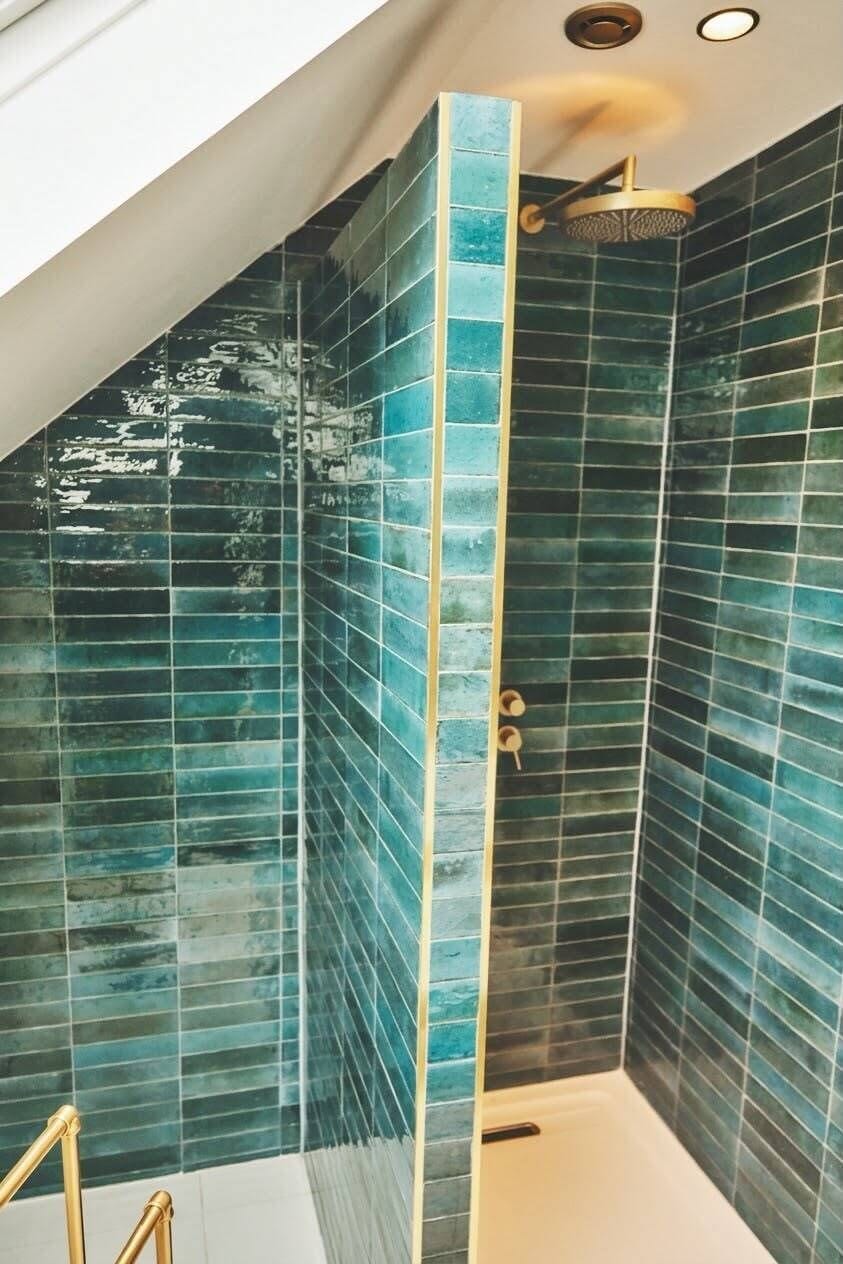 A shower with blue-tiled walls and a gold showerhead.