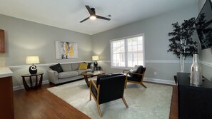 A living room with a grey sofa, a black armchair, a coffee table, and a ceiling fan. - Modern Sleek 2BR Townhome with Garage (Johnson City)