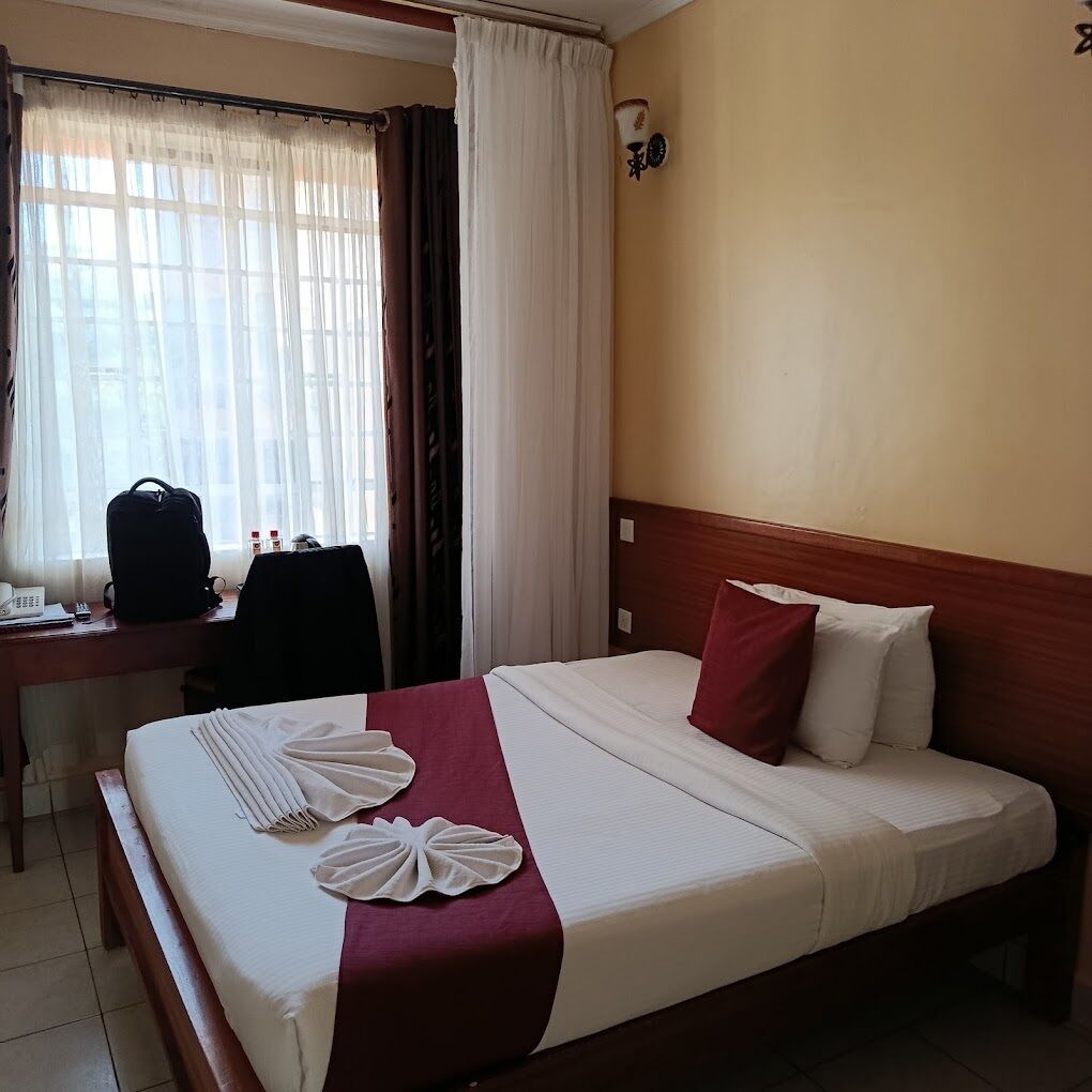 Una habitación de hotel con cama, escritorio, silla y ventana con cortinas.